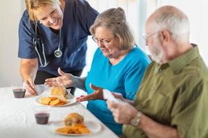 Female Doctor or Nurse Serving Senior Adult Couple Sandwiches at Table photo