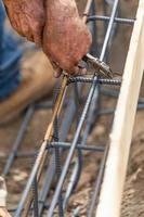 Worker Securing Steel Rebar Framing With Wire Plier Cutter Tool At Construction Site photo