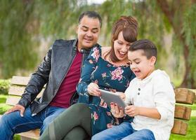 Caucasian Mother and Hispanic Father Using Computer Tablet With Mixed Race Son Outdoors photo