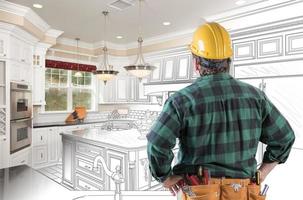 Male Contractor with Hard Hat and Tool Belt Looking At Custom Kitchen Drawing Photo Combination On White.