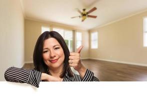 Hispanic Woman with Thumbs Up In Empty Room of House photo