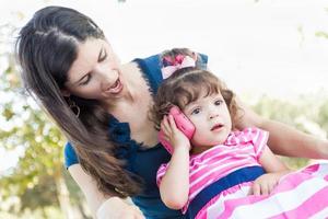 Mixed Race Mother and Cute Baby Daughter Playing with Cell Phone in Park. photo