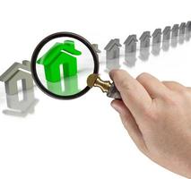 Hand Holding Magnifying Glass Up to Green House in Row of Houses On White photo