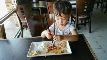 lindo joven chino y caucásico aprendiendo a usar palillos en el restaurante foto