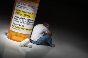 Man Holding Head Sitting Next To Hydrocodeon Pills and Bottle photo