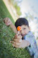 Young Boy Enjoying His Lollipop Outdoors Laying on Grass photo