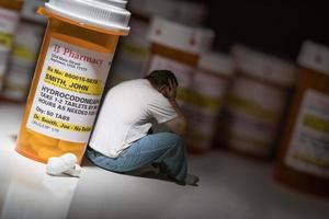 Man Holding Head Sitting Next To Hydrocodeon Pills and Bottle photo