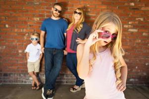 Cute Young Caucasian Girl Wearing Sunglasses with Family Behind photo