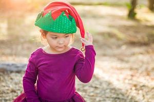 Una linda niña de raza mixta divirtiéndose usando un sombrero de navidad al aire libre foto