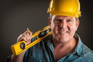 Smiling Contractor in Hard Hat Holding Level and Pencil With Dramatic Lighting. photo