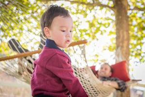 niño de raza mixta divirtiéndose afuera mientras los padres miran desde atrás en una hamaca foto