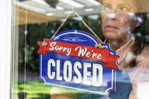 Sad Female Store Owner Turning Sign to Closed in Window photo