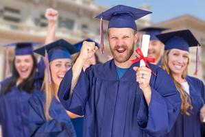 orgulloso graduado masculino con toga y birrete frente a otros graduados foto