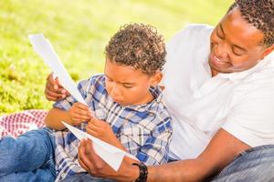 Happy African American Father and Mixed Race Son Playing with Paper Airplanes in the Park photo