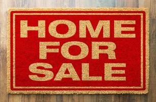 Home For Sale Welcome Mat On A Wood Floor Background photo