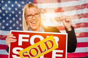 Young Woman Holding House Keys and Sold Sign In Front of American Flag photo