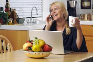 mujer en la cocina con teléfono celular y computadora portátil foto