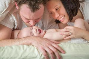 Bebé chino y caucásico de raza mixta acostado en la cama con sus padres foto