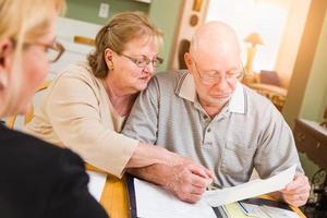 pareja de adultos mayores revisando documentos en su casa con un agente al firmar foto