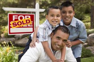 Hispanic Father and Sons in Front of Sold Real Estate Sign photo