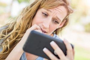 Concerned Young Woman Outdoors Looking At Her Smart Phone. photo