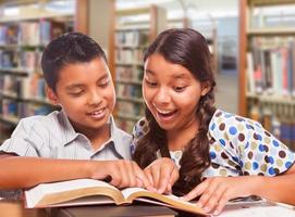 chico y chica hispanos divirtiéndose estudiando juntos en la biblioteca foto