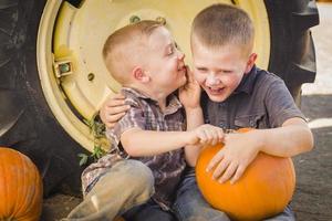 Two Boys Sitting Against Tractor Tire Holding Pumpkins Whispering Secrets photo