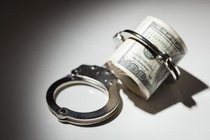 Handcuffs Locked on Roll of One Hundred Dollar Bills Under Spotlight photo