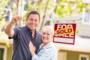 Caucasian Couple in Front of Sold Real Estate Sign and House with Keys photo