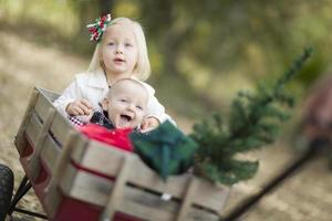 hermanito y hermana tirados en vagón con árbol de navidad foto