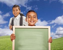 Happy Hispanic Boys In Grass Field Holding Blank Chalk Board photo