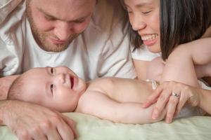 Bebé chino y caucásico de raza mixta acostado en la cama con sus padres foto