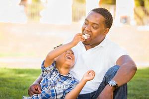padre afroamericano e hijo de raza mixta comiendo una manzana en el parque foto