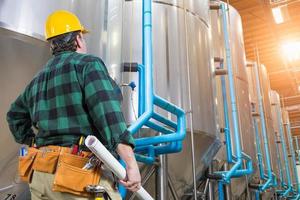 Man Wearing Hard Hat Looking Up At Large Industrial Tanks photo