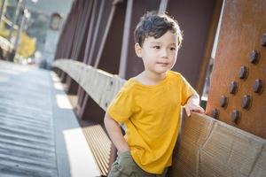 niño de raza mixta apoyándose en el puente al aire libre foto