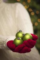 mujer con mitones rojos de temporada sosteniendo adornos navideños verdes foto