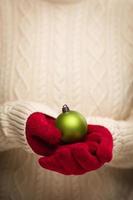 mujer con mitones rojos de temporada sosteniendo adornos navideños verdes foto