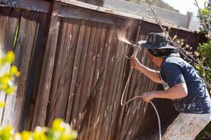 pintor profesional rociando valla de jardín con mancha foto
