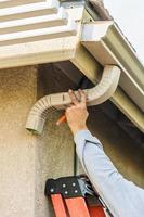 Worker Attaching Aluminum Rain Gutter and Down Spout to Fascia of House photo