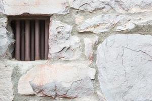Old Stone Wall With Small Iron Barred Prison Cell Window photo