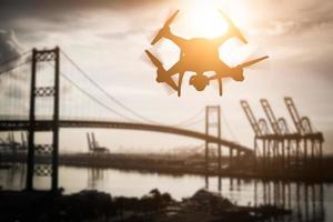 Silhouette of Unmanned Aircraft System Quadcopter Drone In The Air Over Shipping Port. photo