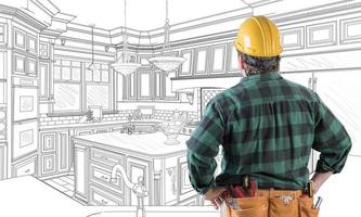 Male Contractor with Hard Hat and Tool Belt Looking At Custom Kitchen Drawing On White. photo