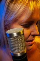 Female vocalist under gelled lighting sings with passion into condenser microphone. photo