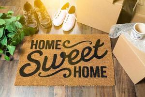 alfombra de bienvenida hogar dulce hogar, cajas de mudanza, zapatos de mujer y hombre y plantas en suelos de madera dura foto