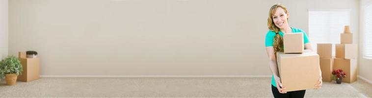 Banner of Happy Young Adult Woman Holding Moving Boxes In Empty Room In A New House. photo