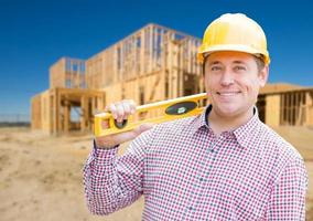 contratista masculino sonriente en casco con planos y nivel en el sitio de construcción de viviendas. foto