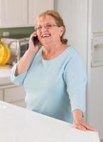 feliz mujer adulta mayor en su teléfono celular inteligente en la cocina foto