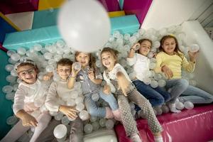 Happy little kids in ball pit smiling happily at camera while having fun photo