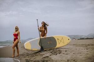 Two young women with paddle board on the beach on a summer day photo