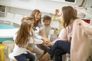 lindos niños en edad preescolar se dan la mano con su maestra de guardería foto